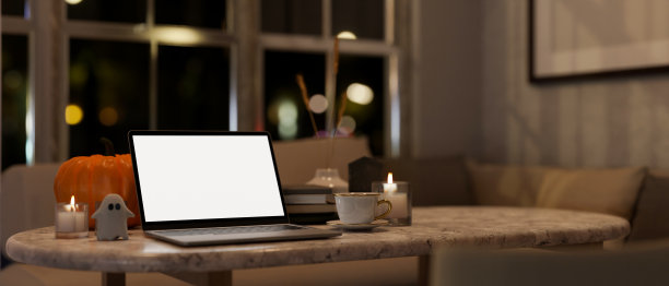 夜晚的家庭工作空间以万圣节为主题，房间里的桌子上放着一台白屏笔记本电脑模型。图片下载
