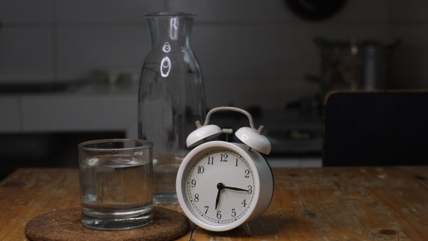 闹钟的概念照片，一个杯子和一瓶水在黑暗的背景，图片下载
