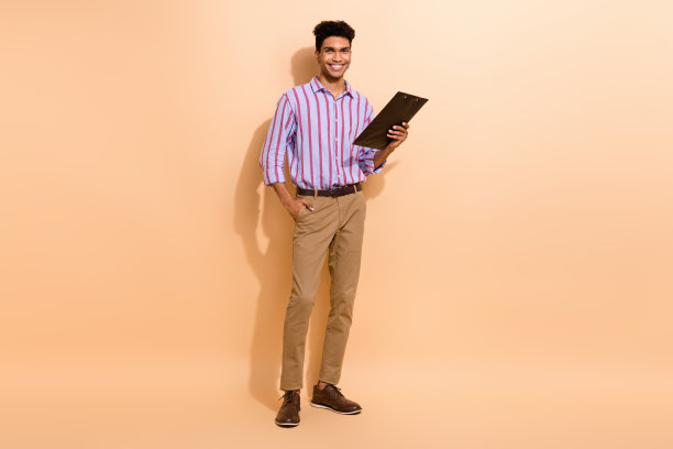 全尺寸照片，自信英俊的男人穿着条纹衬衫棕色裤子，把空白的手放在口袋里孤立的米色背景图片下载