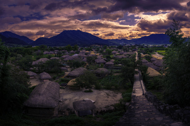 顺天市旅游公司拍摄的韩国全罗南道传统韩屋小镇——长庵邑城民俗村的照片，在一片片稻草屋顶和青山的映衬下，落日的云景引人注目图片下载