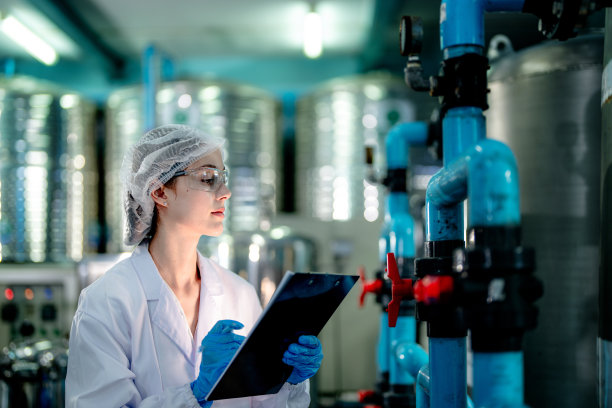 工业工厂的科技工人在检查反渗透机系统的质量。女工在控制面板上记录数据，测量便携式回收装置的压力。图片下载