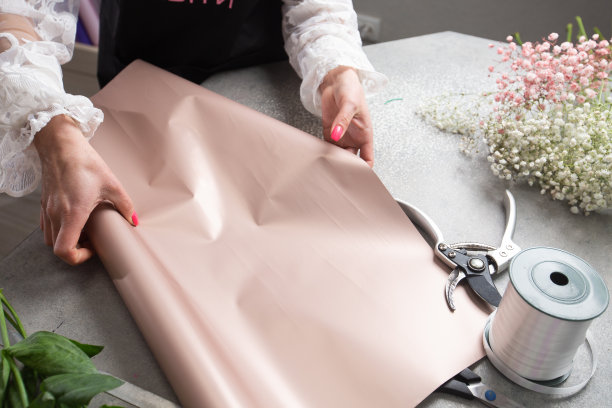 女花商包装美丽的花束与纸在桌子上，在桌面上俯瞰。高质量的照片图片下载