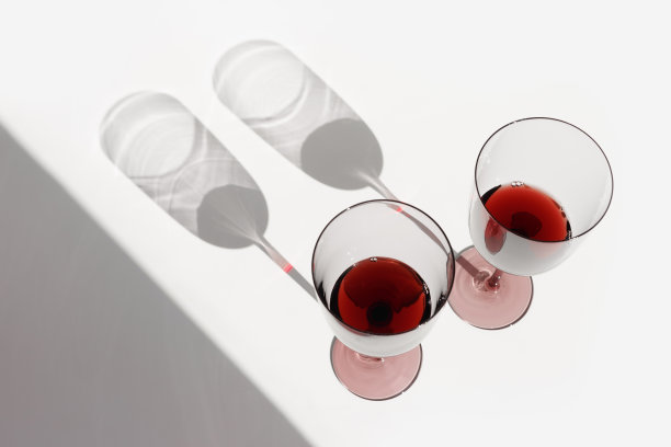 最小的夏日场景与一杯红酒，阳光的阴影在白色的背景，copyspace，酒杯平放。两个酒杯，酒精饮料的照片。假期，聚会，活动的概念图片下载