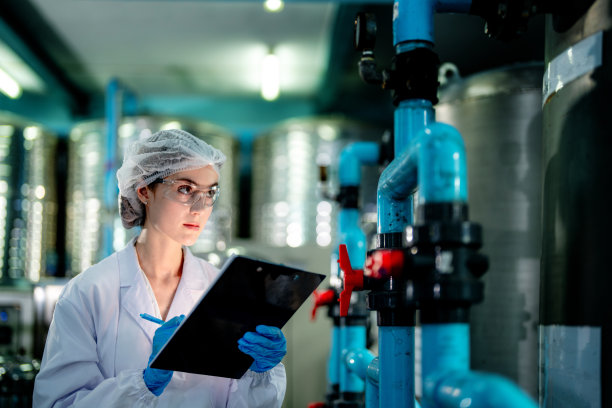 工业工厂的科技工人在检查反渗透机系统的质量。女工在控制面板上记录数据，测量便携式回收装置的压力。图片下载