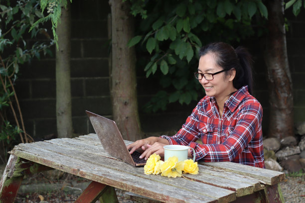 一位女农民正拿着搪瓷咖啡杯在笔记本电脑前工作。在家里的花园里做网上生意的女人。生活照片。图片下载