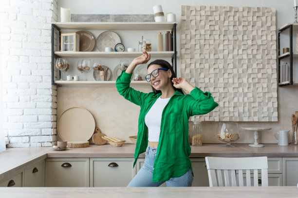 年轻的梦想和快乐的女人在家里的厨房里跳舞。举起她的手，闭上她的眼睛，听音乐，快乐图片下载