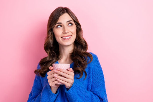 漂亮的年轻女孩的照片肖像拿着咖啡杯看起来空的空间穿着时尚的蓝色衣服孤立在粉红色的背景图片下载