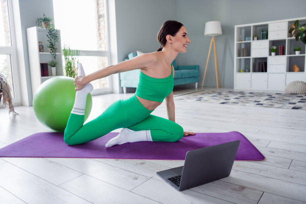 开朗的漂亮女孩穿着运动服在家里观看网络课堂设备伸展腿的照片图片下载