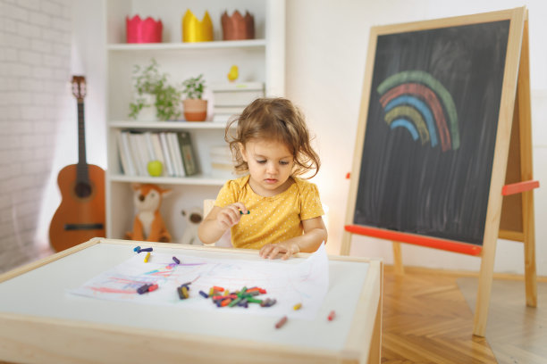 小女孩坐在椅子上用彩色蜡笔画画。图片下载