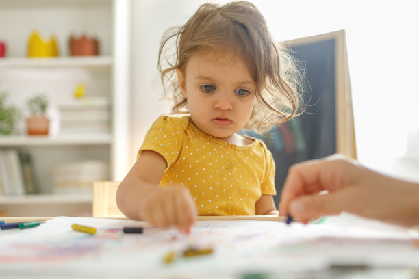 小女孩坐在椅子上用彩色蜡笔画画。图片下载