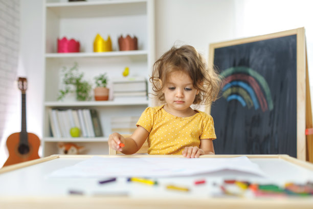 小女孩坐在椅子上用彩色蜡笔画画。图片下载