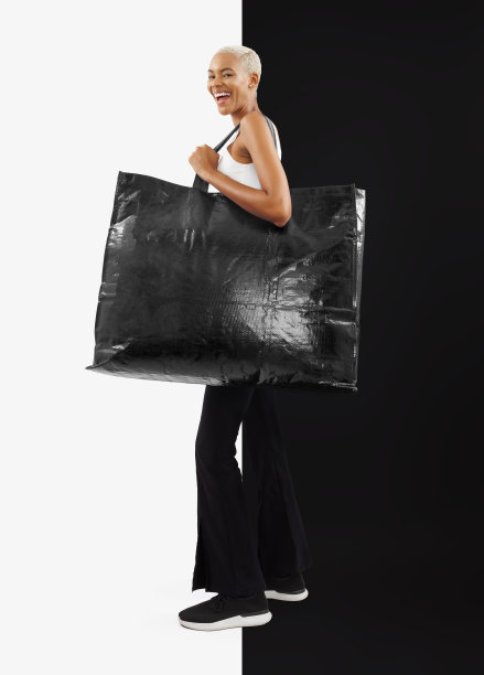 黑色星期五购物。笑，快乐，微笑的黑人妇女穿着休闲服装，拿着一个大的黑色购物袋，上面有文字的复制空间。空白的背景图片下载