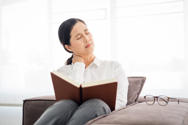 疲惫、紧张、年老、成熟的女商人，患有纤维肌痛、颈痛，在家里客厅的沙发上看书。高级中年女士按摩颈部，感觉因阅读而疼痛。图片下载