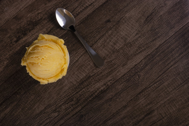 美味的黄色奶油冰淇淋装在白色的碗里，旁边放着勺子。顶部照片，元素位于图像的左上角，右侧为空白区域。冰淇淋球。图片下载