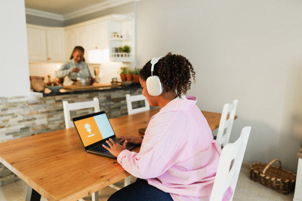 非裔美国女儿使用笔记本电脑，而母亲在家里做饭的背景-家庭生活方式的概念-主要关注耳机图片下载