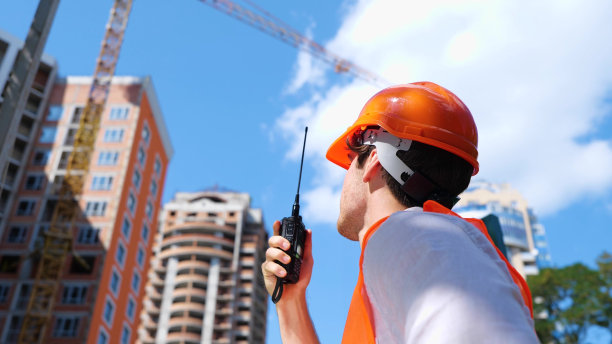 男建筑工人在工地外站着，拿着对讲机。商业、建筑、行业理念。慢动作图片下载