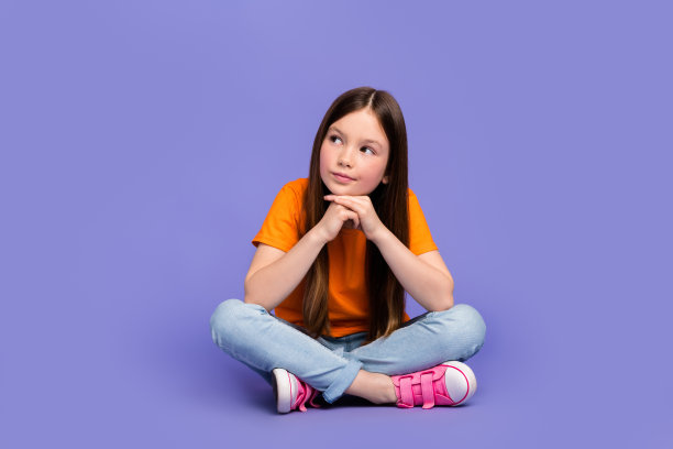 智能思考学生穿着橙色t恤的全长照片，坐在紫色的背景上看空提供孤立图片下载