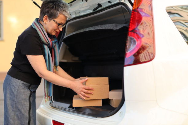 非接触式购物和安全送货:女人把货物装在汽车后备箱里，蒙面和快乐。图片下载