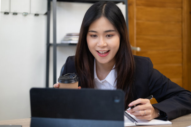 头部照片微笑的女性成功的亚洲国际公司工作人员坐在桌子前的电脑，查看客户的电子邮件。快乐的女商人在笔记本电脑应用程序项目工作。图片下载