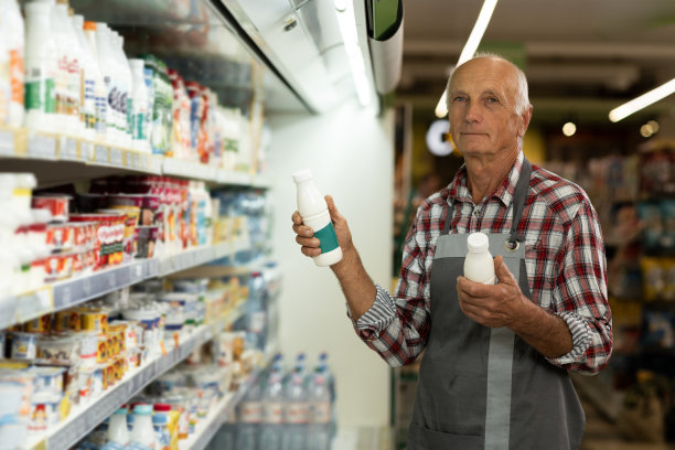 一个面带微笑的老工人，系着围裙，拿着超市里的奶制品图片下载