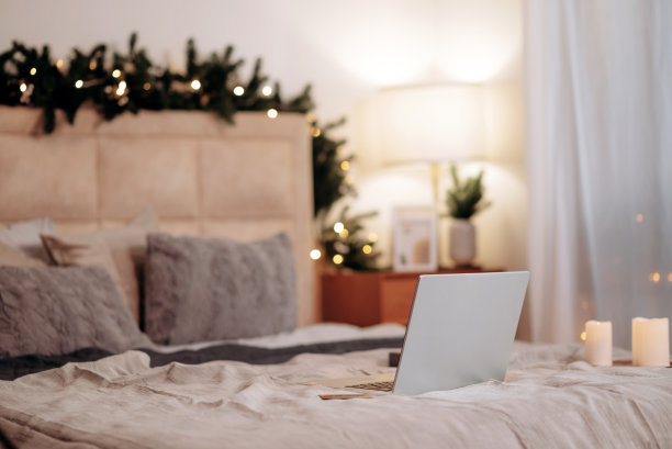 打开的笔记本电脑躺在卧室的床上，家里装饰着圣诞装饰。自由的概念图片下载