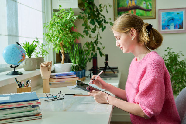 十几岁的女学生插画家坐在家里的书桌上，在数字平板电脑上画画图片下载