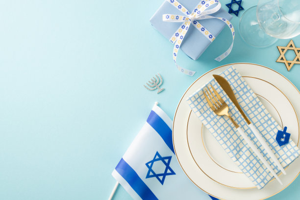 光明节在一张俯视图照片中，展示了一张桌子，上面摆放着盘子、餐具、餐巾、酒杯、大卫之星、礼物、以色列国旗，背景是淡蓝色的文字空间图片下载