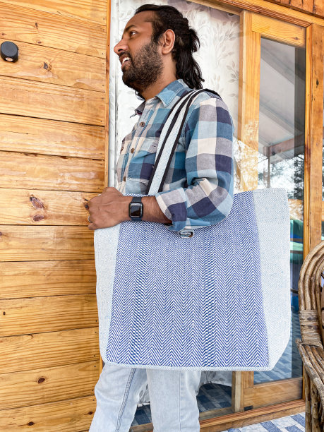 印度男子的特写照片，肩上背着购物大手提袋，走过木制的海滩小屋，穿着休闲服装蓝白格子衬衫，牛仔裤，侧视图，重点在前景图片下载