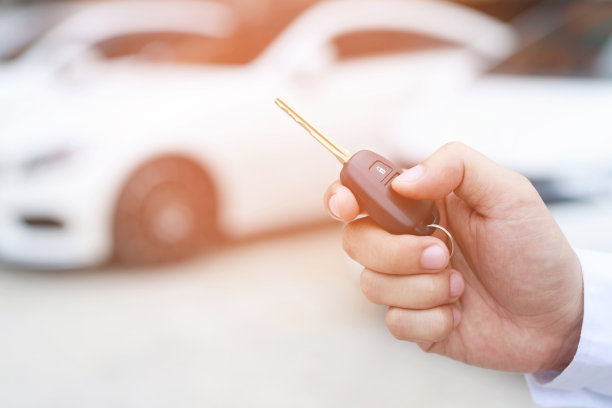 车钥匙，商人把钥匙交给展厅背景的另一个人。卖方经销商信用利息支付或分期购车的概念。图片下载