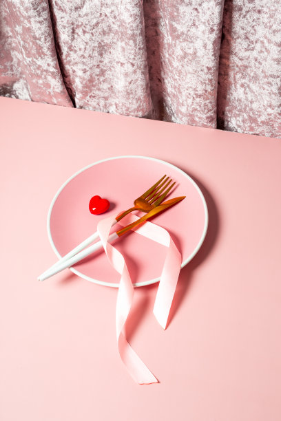 情人节的桌子设置在粉红色的背景，垂直照片与copyspace。粉红色的盘子，金色的餐具和红色的心顶视图，浪漫的晚餐概念图片下载