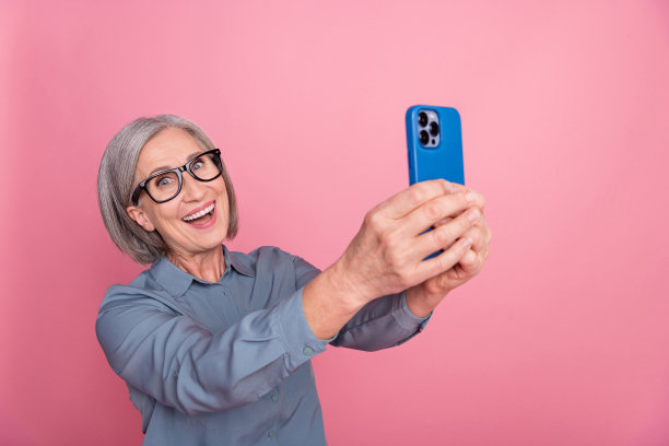 照片正面可爱的资深女士穿着时尚的衣服拿着iphone说话在线流媒体拍摄孤立的粉红色背景图片下载