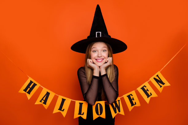 漂亮的金发少女的照片肖像兴奋装饰花环穿着黑色万圣节服装孤立的橙色背景图片下载