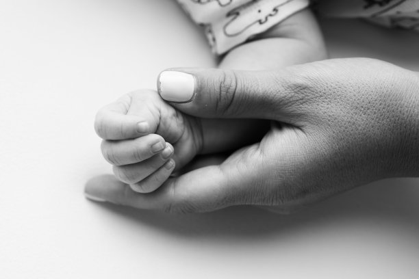 父母的手握着新生婴儿的手指。一对父母的手握着一个新生婴儿的拳头(特写)。家庭保健和医疗保健。黑白照片里小小的手指。图片下载