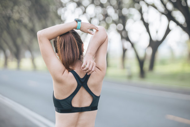 年轻女性在公园健身训练前正在锻炼。健康的年轻女子在户外热身。她伸伸胳膊，看向别处，嗨，key。图片下载