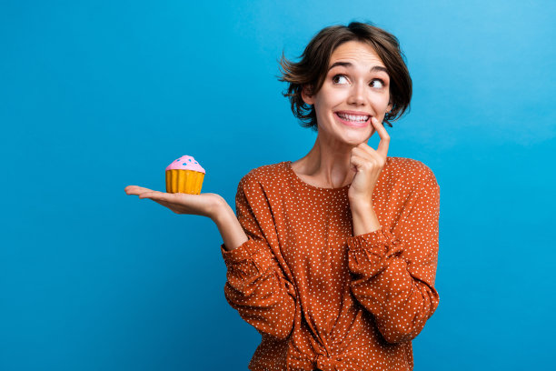 照片上的年轻美女纸杯蛋糕看起来好奇的空空穿着时髦的棕色衣服孤立在蓝色的背景图片下载