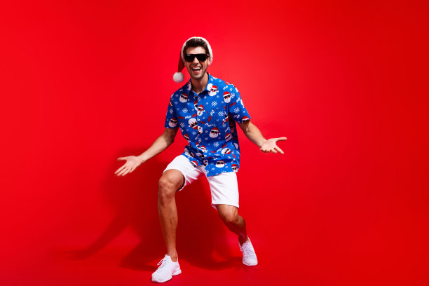 漂亮的年轻男子的全身照片时髦的舞蹈有乐趣迪斯科穿圣诞老人印花圣诞服装孤立的红色背景图片下载