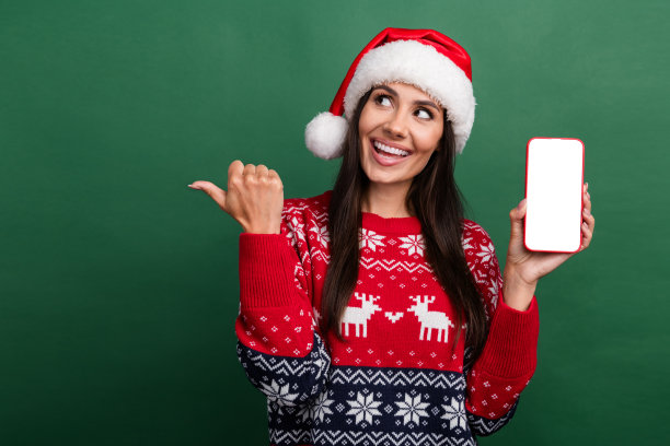 照片中闪亮兴奋的女圣诞精灵穿着装饰圣诞套头衫，显示装置空旷孤立的绿色背景图片下载