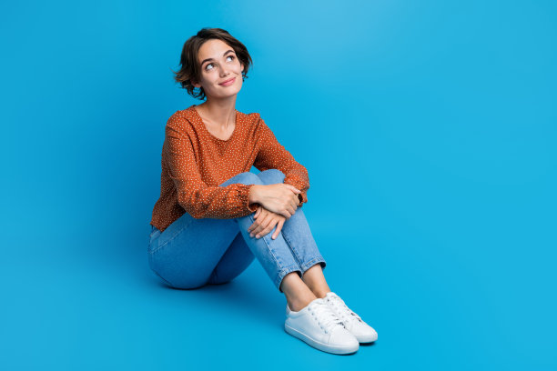 年轻的女士模特的全身视图照片坐在地板上梦幻的脸穿着休闲服装孤立的蓝色背景图片下载