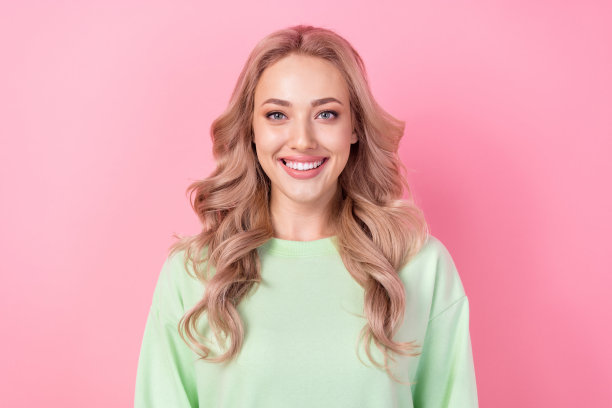 乐观可爱的女孩穿着时尚的绿色运动衫的肖像照片，有牙齿的微笑模特金发女郎孤立在粉红色的背景图片下载
