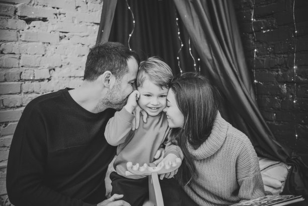 家庭度假的概念。母亲、父亲在家拥抱儿子。新年快乐，圣诞快乐。妈妈，爸爸，拥抱孩子。圣诞树，装饰室内。黑白照片特写。图片下载