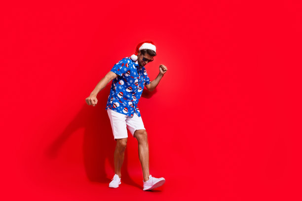 全身照片英俊的年轻人跳舞迪斯科舞厅穿着圣诞老人印刷圣诞服装孤立的红色背景图片下载