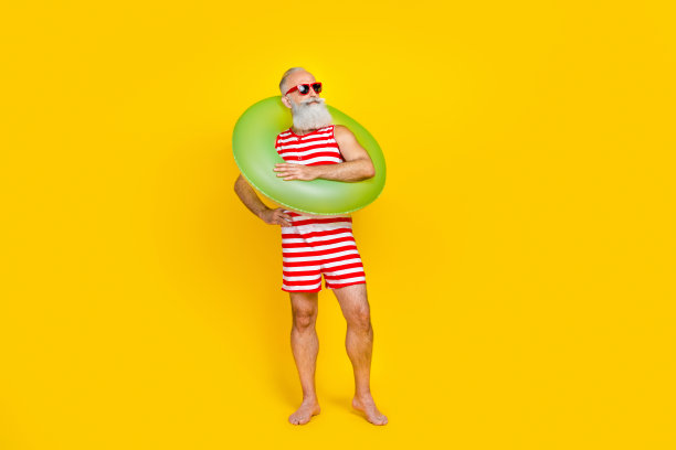 照片正面梦幻的老人穿着条纹红色的泳衣拿着漂浮的浮标看着空的空间孤立的黄色背景图片下载