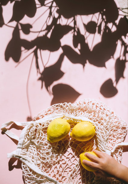 照片有机柠檬水果在网袋在浅粉红色的背景。完全不完美的柠檬图案。天然食品。新潮的阳光，简约的风格。图片下载