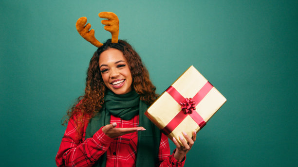 兴奋的年轻女子朝圣诞礼物做手势，手掌朝上，摄影棚里的照片图片下载