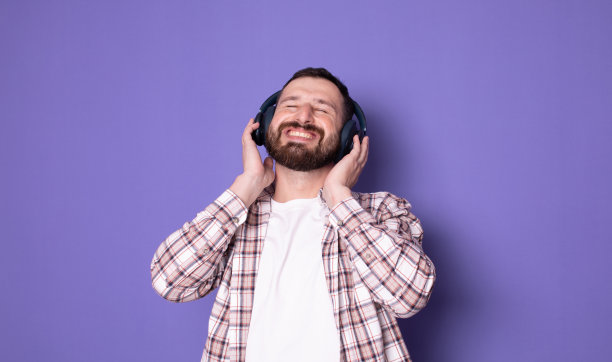 英俊的大胡子男人快乐积极地戴着耳机听音乐。图片下载