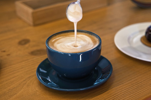 手正在搅拌拿铁的奶泡。用钢勺搅拌卡布奇诺。热咖啡在白色经典陶瓷杯在木桌。现代咖啡店，自助餐厅。厚的泡沫。特写镜头图片下载