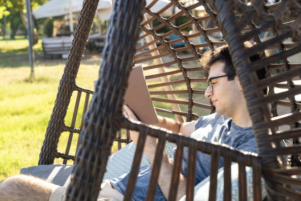 年轻男人坐在吊床上看书照片图片下载