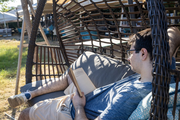 年轻男人坐在吊床上看书照片图片下载