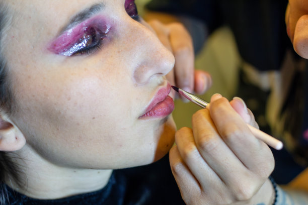 年轻女子正在化妆室里接受专业化妆师的化妆，嘴上涂着口红图片下载