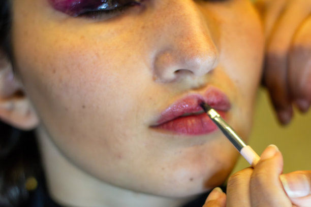 年轻女子正在化妆室里接受专业化妆师的化妆，嘴上涂着口红图片下载